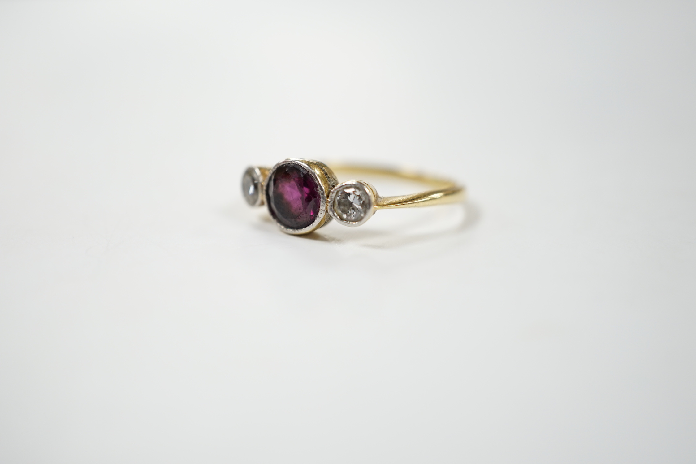 An early 20th century yellow metal and millegrain set single stone garnet and two stone diamond ring, size M, gross weight 2.8 grams.